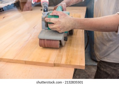 Using a hand-held sanding machine or belt sander to level the surface of a sheet of plywood for a cabinet, table or other furniture at a workshop. - Powered by Shutterstock