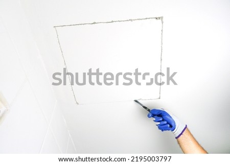 Using a handsaw cutting to cut a hole in the ceiling to install the service port.	        