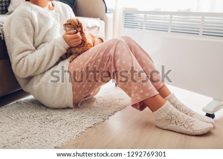Using heater at home in winter. Woman warming body with cat. Heating season.