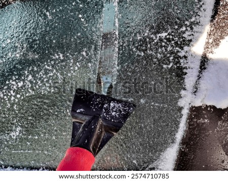 using ice scraper to clean car windshield after winter snow and ice storm 