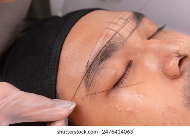 Using inked threads to make guide lines around the eyebrows of a male patient to get te exact measurements for microblading procedure.