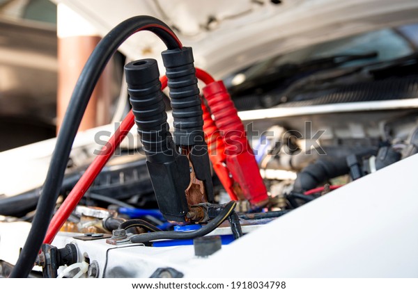 Using Jumper\
Cables To Charge A Dead Car Battery. Technician charging the\
battery with Electric Charge Cable\
set.