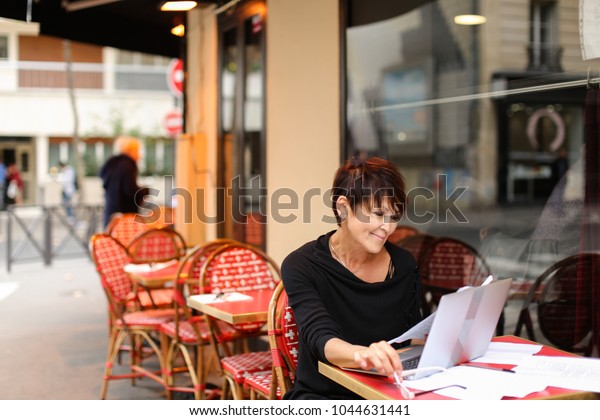 using laptop aged tired woman bank employee writing financial plan for several hours. Lady hold reports in left hand and printing last items in computer. Finishing, female wear glasses with conte