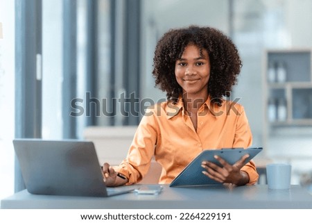 Using laptop computer, Young pretty african american business woman bookkeepers working with balance sheet yearly reports to calculate tax and online consult in modern office.