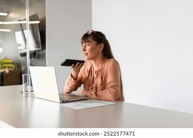 Using laptop and holding smartphone, woman working from home office desk. Remote working, technology, business, multitasking, digital, lifestyle - Powered by Shutterstock