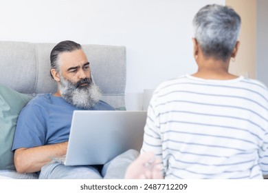 Using laptop, senior man working from bed while talking to partner. Remote working, telecommuting, technology, business, home office, communication - Powered by Shutterstock