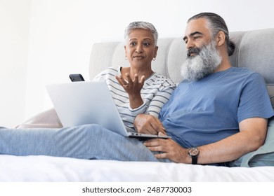 Using laptop and smartphone, senior couple relaxing on bed and discussing something. Technology, relaxation, communication, bedroom, conversation, lifestyle - Powered by Shutterstock