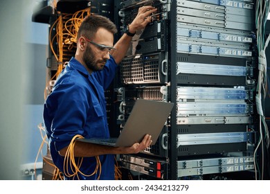 Using the laptop. Young man is working with internet equipment and wires in server room. - Powered by Shutterstock - Get 15% off with code: PIKWIZARD15