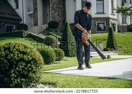 Using leaf blower. Professional gardener is on the lawn.