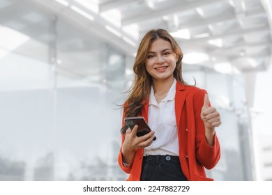 Using mobile, call phone, Smiling young Asia business woman leader entrepreneur in red color suit working outdoor urban street walk. - Shutterstock ID 2247882729