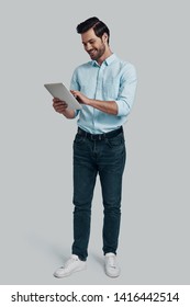 Using Modern Technologies. Full Length Of Young Man Working Using Digital Tablet While Standing Against Grey Background