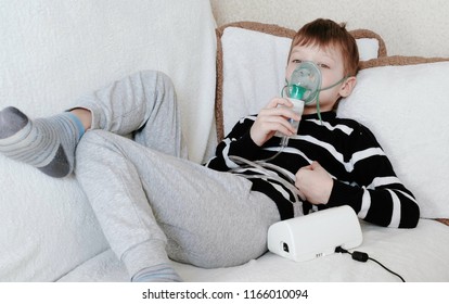 Using nebulizer and inhaler for the treatment. Boy inhaling through inhaler mask lying on the couch.