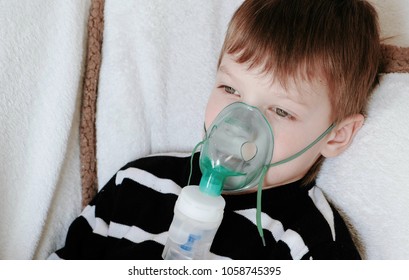 Using nebulizer and inhaler for the treatment. Boy's face inhaling through inhaler mask lying on the couch.