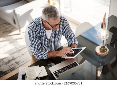 Using Online Tools To Manage And Analyze Financial Accounts. High Angle Shot Of A Mature Man Working On A Digital Tablet At Home.