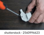 Using a Phillips screwdriver, loosen the screw on the white electrical power plug, close up. The process of parsing the body of plastic electrical plug. Repair and maintenance of electrical equipment