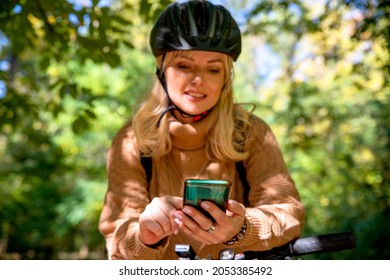 Using phone in forest for orientation. Female cyclist looking at gps map application in green Park. Selective focus on the smart phone in hands