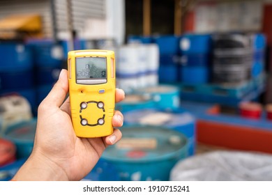 Using A Portable Gas Detector To Monitor The Air Or Toxic Gas Composition Around The Chemical Storage Area (with Blurred Background Of Chemical Barrel). Industrial Action And Object Photo.