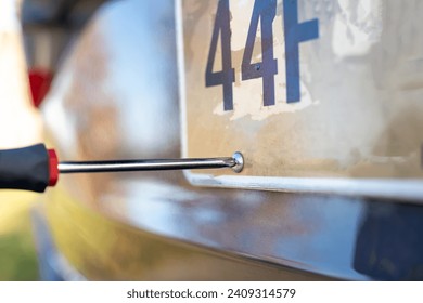 Using a screw driver to remove and replace a vehicle rear license plate. 