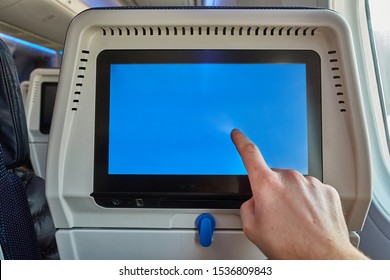 Using the seatback screen on a plane trip, watching movies, displaying flight data. Finger on blank touchscreen.