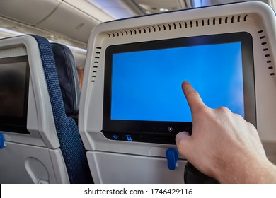 Using the seatback screen on a plane trip, watching movies, displaying flight data. Finger on blank touchscreen.