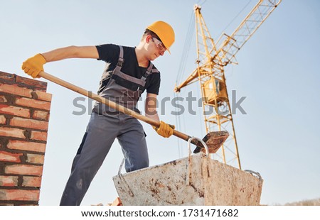 Using showel. Construction worker in uniform and safety equipment have job on building.