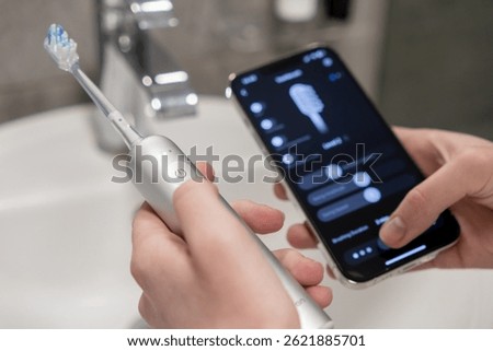 Using a smartphone app to control and manage settings on an electric toothbrush, hands demonstrate advanced personal oral hygiene management through integrated technology for optimal health results