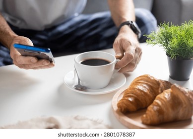 Using Smartphone During Breakfast with Coffee and Croissants on White Table