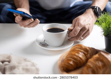 Using Smartphone During Breakfast with Coffee and Croissants on White Table