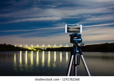 Using smartphone like professional camera on tripod to capturing night landscape with a lot of lights reflected on surface of the water