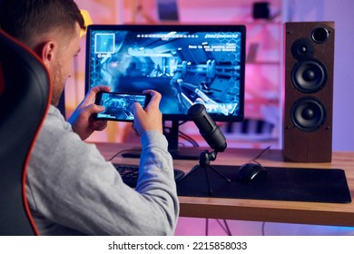 Using the smartphone. Online streamer playing FPS shooter game at home.