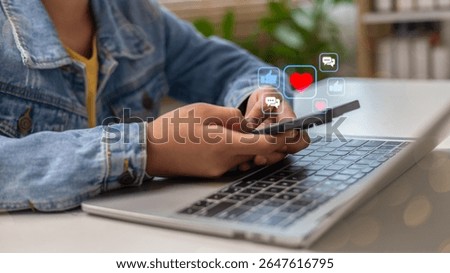 Using a smartphone while a laptop is open, with social media icons floating, such as likes, hearts, and comments, representing online interaction and digital lifestyle.