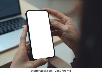 Using smartphone, white screen mockup. Woman using mobile phone with blank white screen during working with laptop on table, mockup for social media marketing ads
