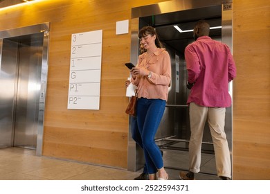 Using smartphone, woman walking past man entering elevator in office building. Technology, business, corporate, hallway, communication, professional - Powered by Shutterstock