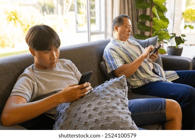 Using smartphones, father and son sitting on couch in living room. Family, technology, bonding, togetherness, parenting, lifestyle - Powered by Shutterstock