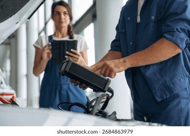 Using special device to check the electronics. Particle close up view of male and female mechanics that are repairing the car.