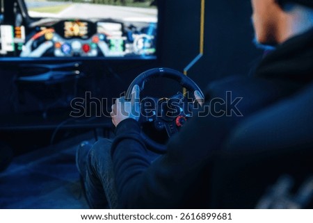 Using steering wheel. Young guy is playing racing game by using driving simulator.