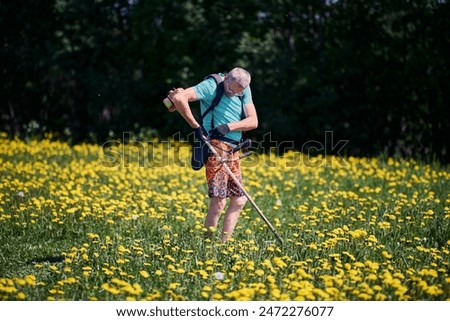 Using suspension to attach gasoline-powered string trimmer before destroying dandelions in local area.