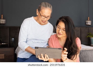 Using tablet,  asian grandmother and granddaughter enjoying time together indoors. family, bonding, technology, multigenerational, happiness, togetherness - Powered by Shutterstock