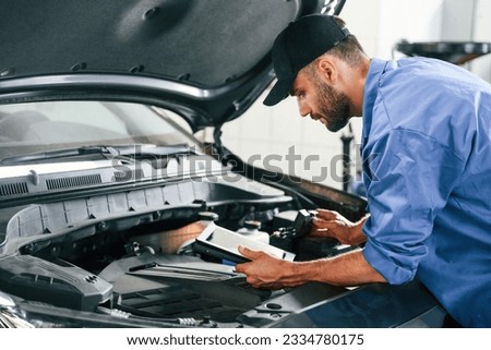 Using tablet. Auto mechanic working in garage. Repair service.