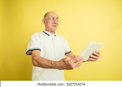 Using Tablet. Caucasian Senior Man's Portrait Isolated On Yellow Studio Background. Beautiful Male Emotional Model. Concept Of Human Emotions, Facial Expression, Sales, Wellbeing, Ad. Copyspace.