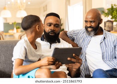 Using tablet, father and son sitting on couch with grandfather smiling. Family, multi-generation, bonding, technology, leisure, happiness - Powered by Shutterstock