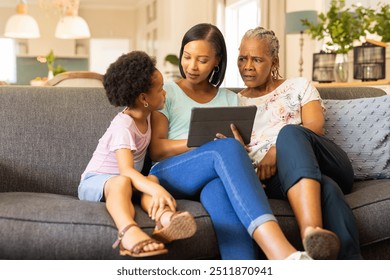 Using tablet, multi-generational family sitting on couch, engaging in conversation. technology, bonding, diverse, living room, communication, interaction, grandmother, daughter, granddaughter - Powered by Shutterstock