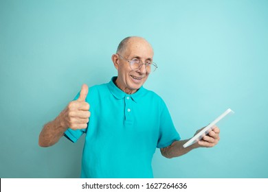 Using Tablet, Thumb Up. Caucasian Senior Man's Portrait On Blue Studio Background. Beautiful Male Emotional Model. Concept Of Human Emotions, Facial Expression, Sales, Wellbeing, Ad. Copyspace.