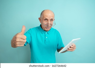 Using Tablet, Thumb Up. Caucasian Senior Man's Portrait On Blue Studio Background. Beautiful Male Emotional Model. Concept Of Human Emotions, Facial Expression, Sales, Wellbeing, Ad. Copyspace.