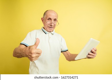 Using Tablet, Thumb Up. Caucasian Senior Man's Portrait On Yellow Studio Background. Beautiful Male Emotional Model. Concept Of Human Emotions, Facial Expression, Sales, Wellbeing, Ad. Copyspace.