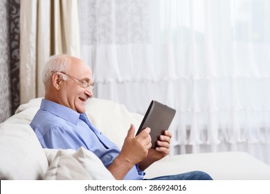 Using Technologies. Portrait Of Old Man Sitting On Couch And Using Tablet.