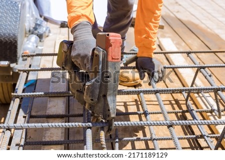 Using this tool, workers twist reinforcement wires with steel bars for cement foundations in construction site