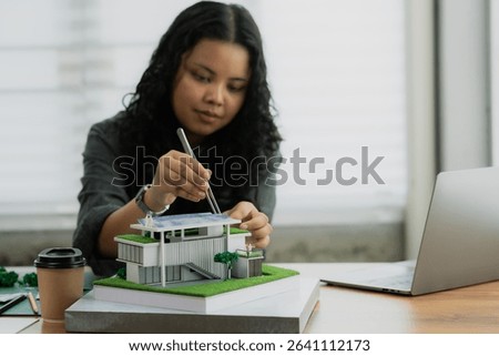 Using tweezers for precision, an architect adds miniature scale figures to the roof of a sustainable house model