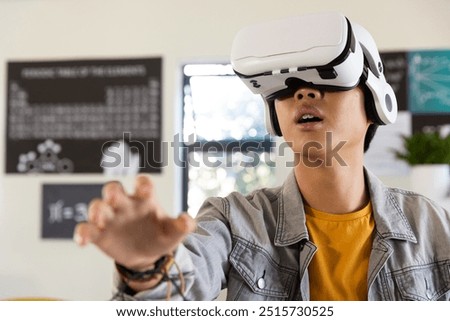 Using virtual reality headset, asian teenage boy exploring digital world in school classroom. Technology, education, learning