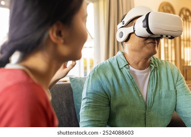 Using VR headset, asian father experiencing virtual reality while woman watching attentively. technology, immersive, interaction, experience, simulation, digital - Powered by Shutterstock